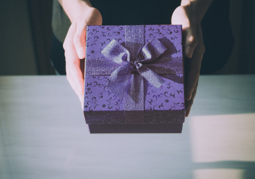 nell'immagine, due mani tengono un pacco regalo blu, decorato con un fiocco dello stesso colore