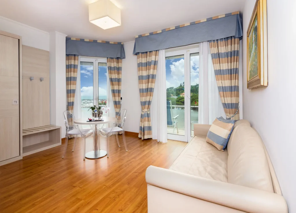 nell'immagine, una camera con pavimento in legno, un divano in pelle bianca sulla destra e due ampie portefinestre che danno sul terrazzo, affacciato sul mare